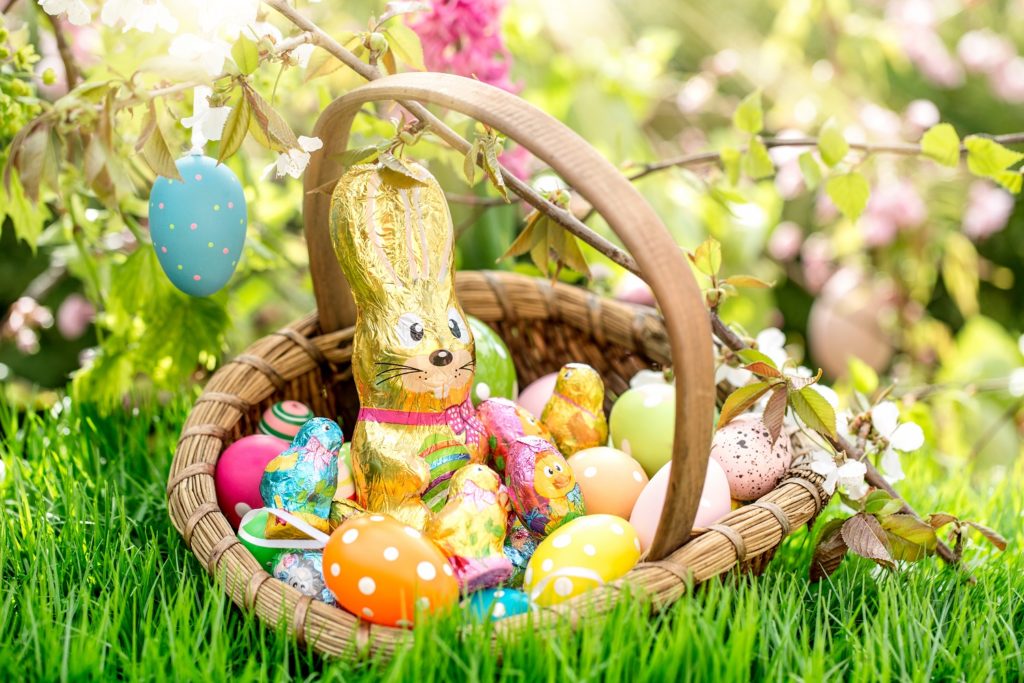 Easter in Alexandria and Pineville: A wicker basket on lush green grass filled with a foil-wrapped chocolate bunny, vibrant Easter eggs, and spring blooms.